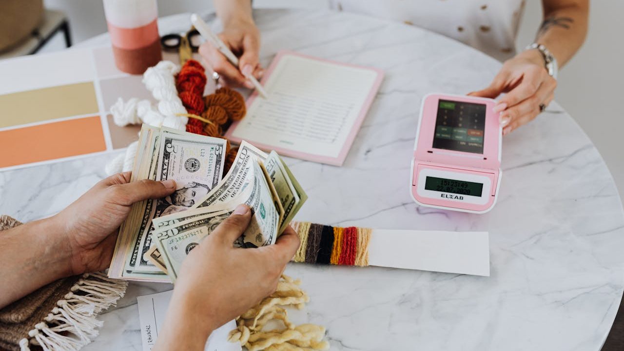 A hand holding US bank notes beside a card payment terminal on a counter — representing card acceptance powered by NMI payments